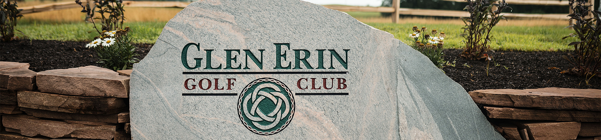Stone sign for Glen Erin Golf Club with decorative elements and flowers in the foreground.