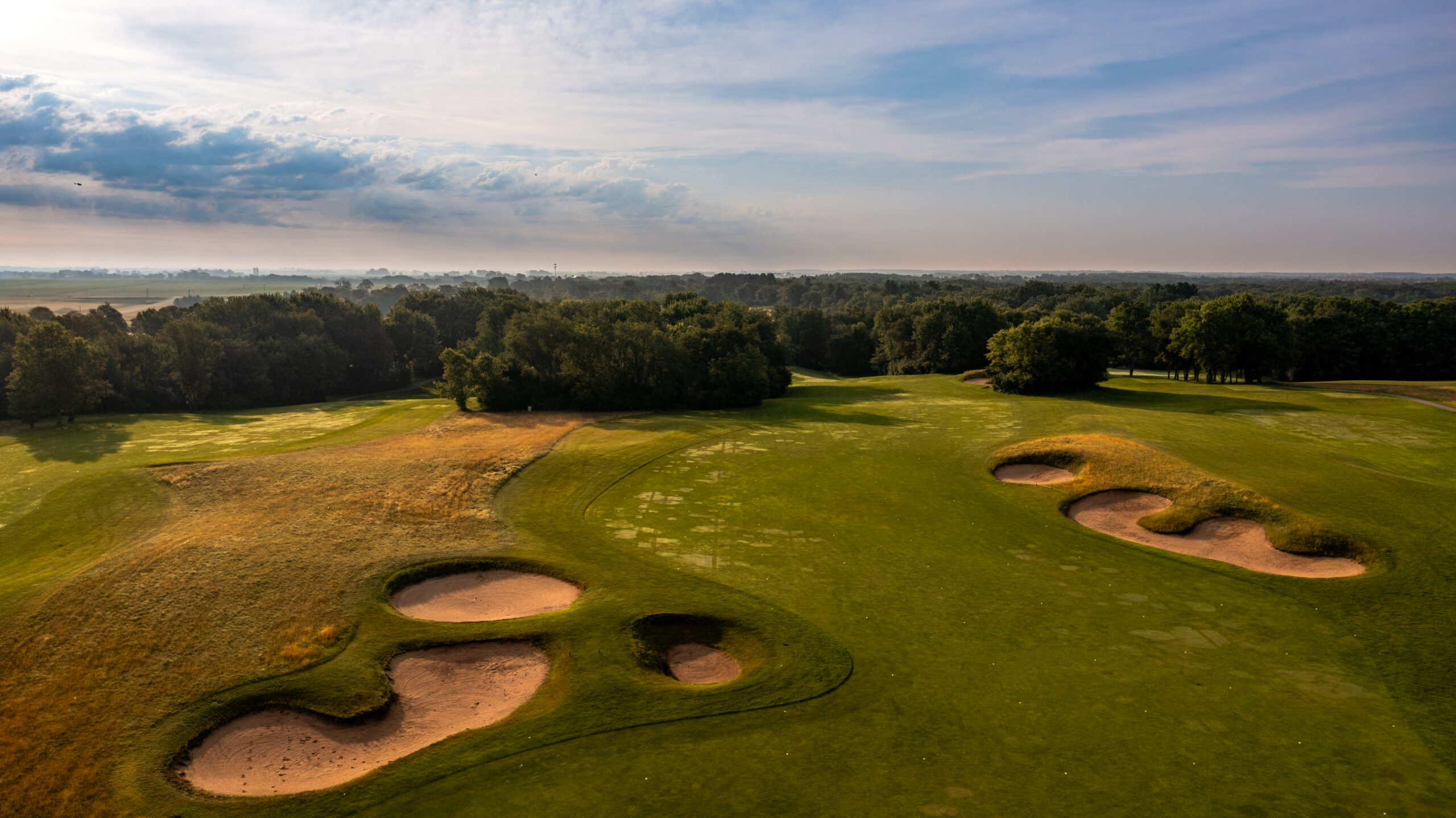 Aerial view of a golf course featuring sand traps and lush green fairways under a cloudy sky.