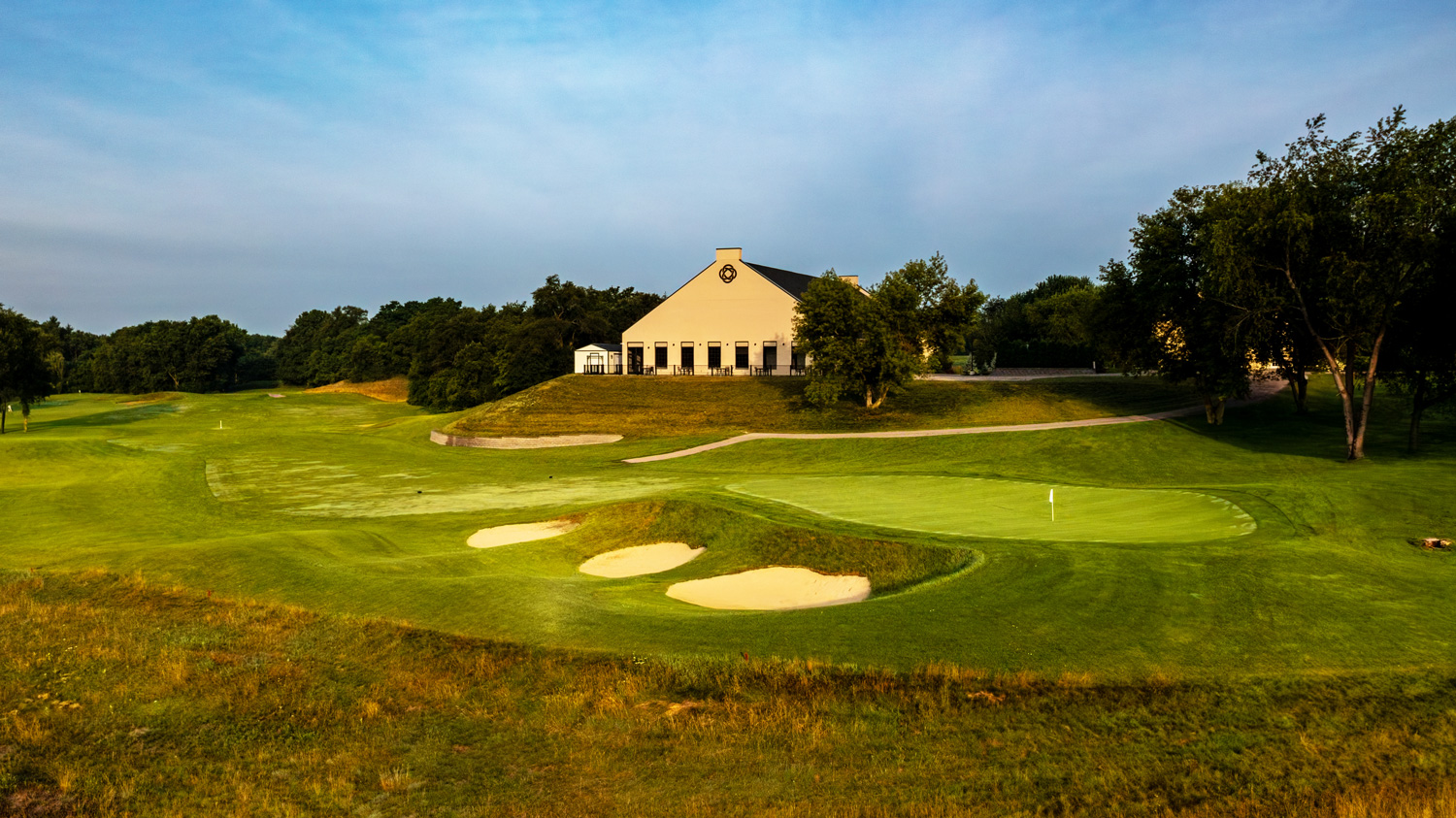 A scenic view of a golf course with a clubhouse in the background, featuring sand traps and lush green grass.